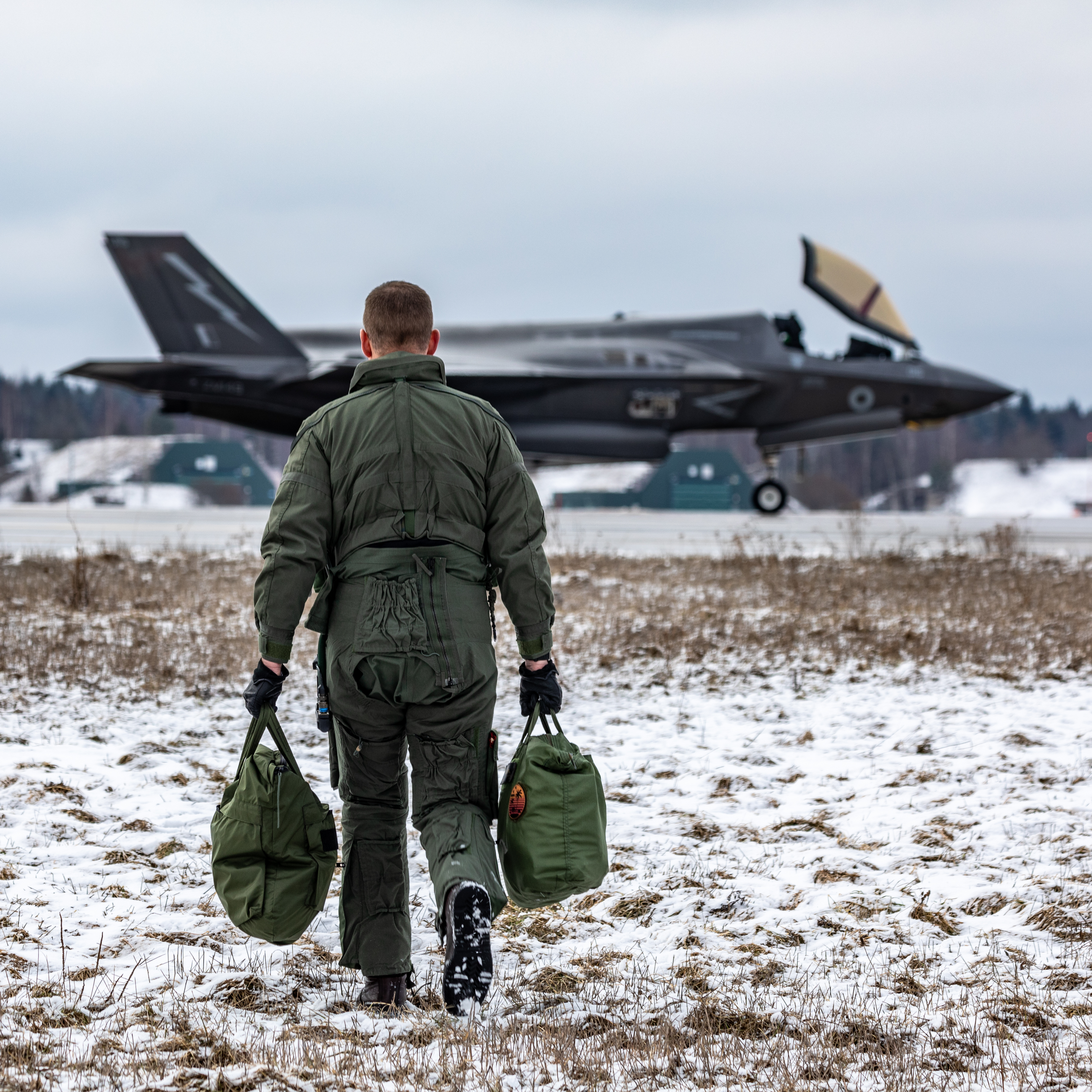 Personnel carries baggage towards Lightning aircraft.